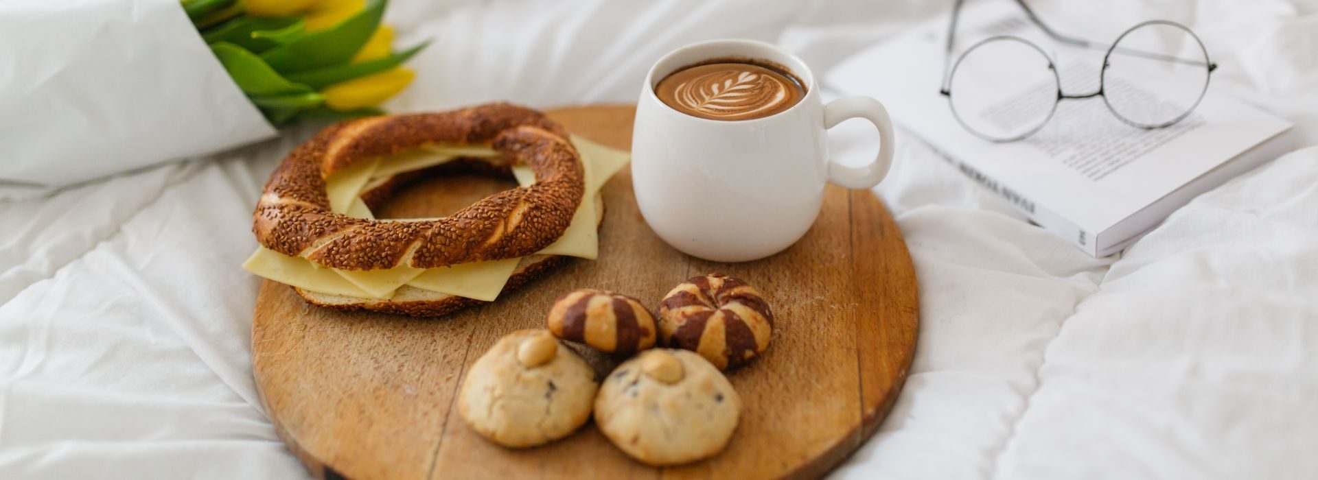 Breakfast in bed with rolls, cheese, cookies and hot beverage on a wooden tray.