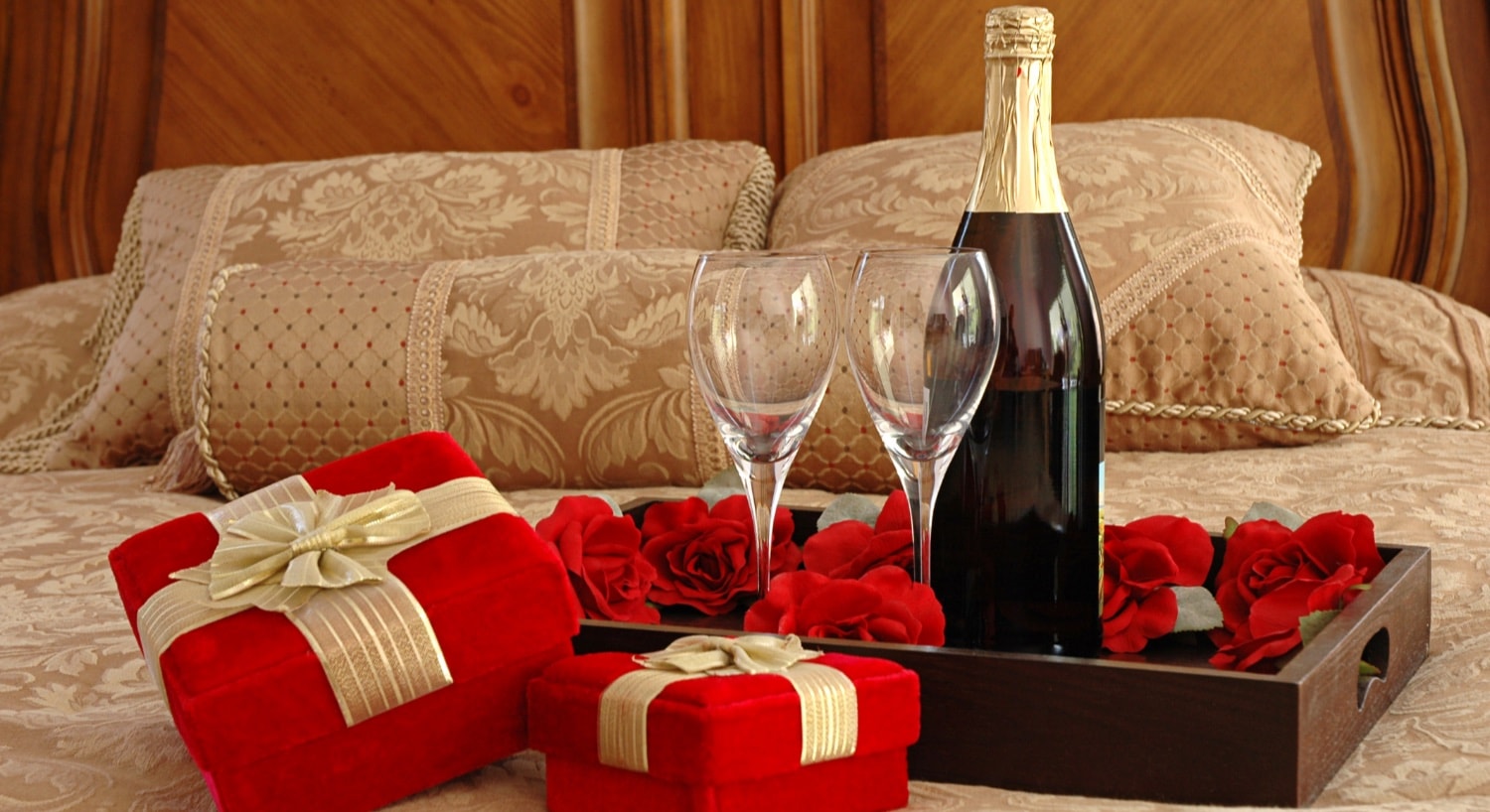 Wine glasses and bottle of wine in tray on bed