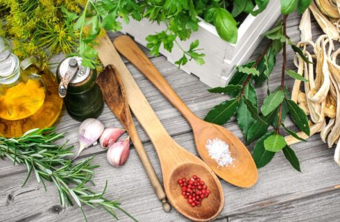 Herbs, shallots, wooden spoons, olive oil, and pepper grinder on table top