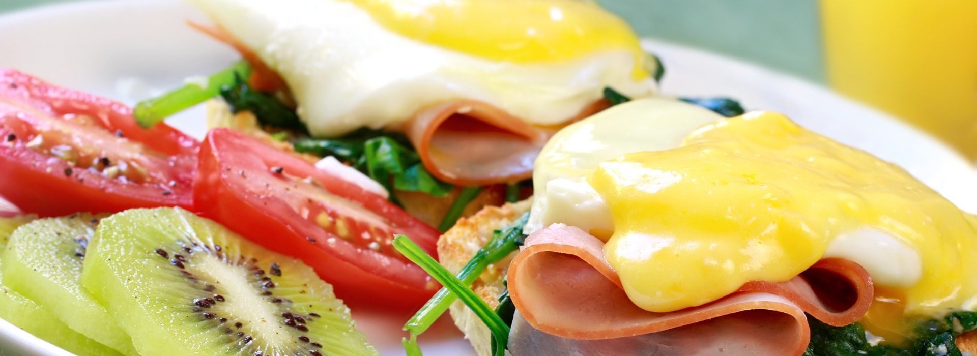 Close up view of eggs benedict with sliced tomatoes and kiwi