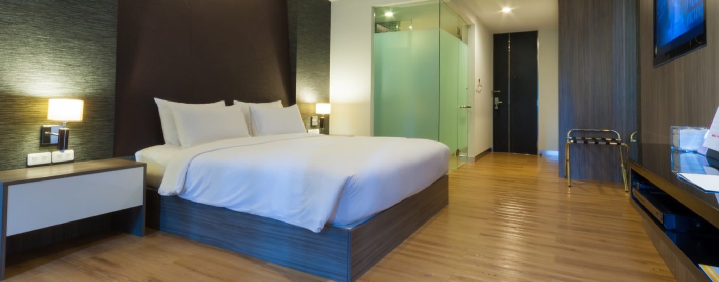 Bedroom with dark wooden paneling, light brown hardwood flooring, and platform bed with white bedding