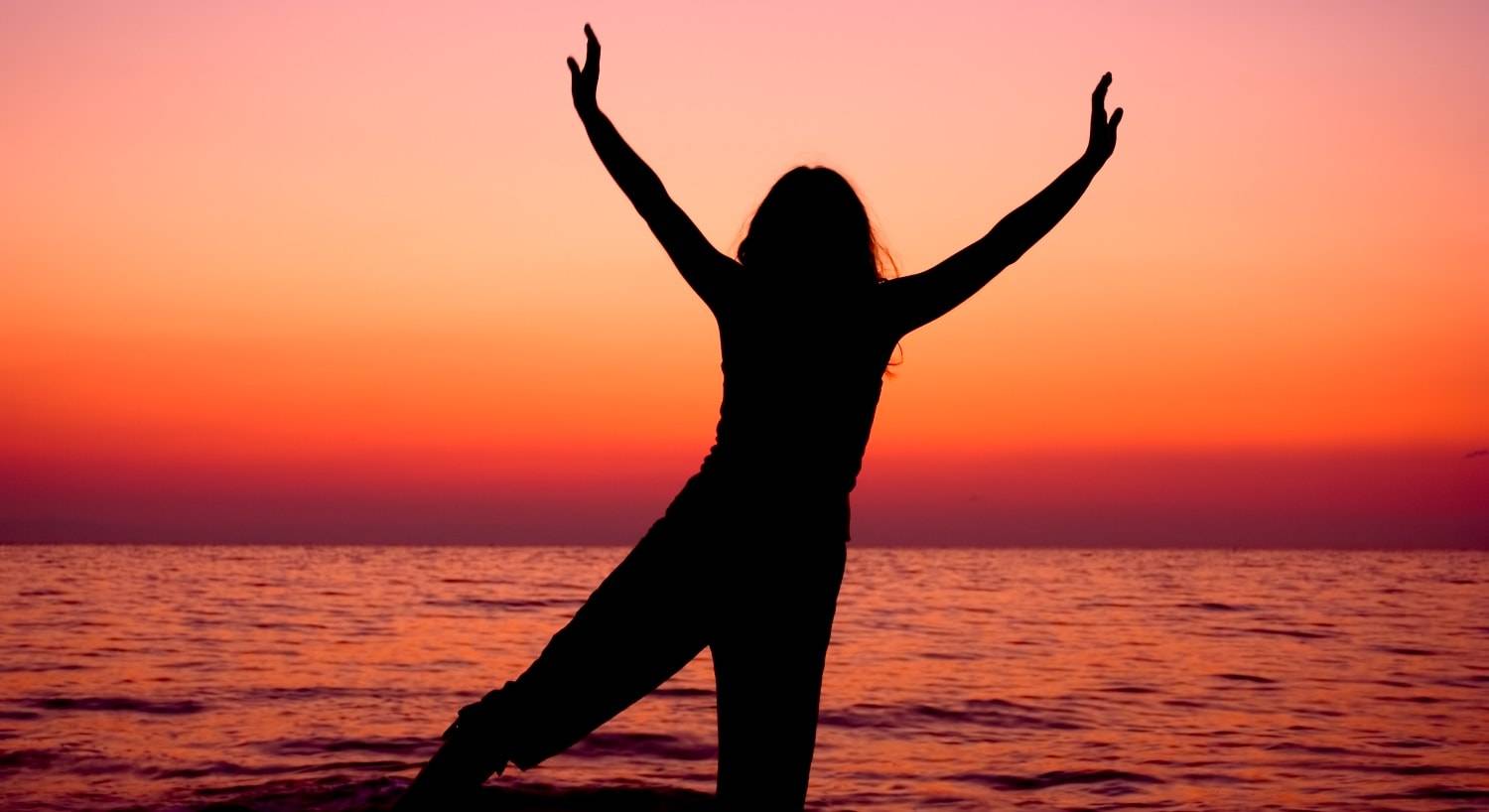 Silhouette of woman posing near body of water at sunset