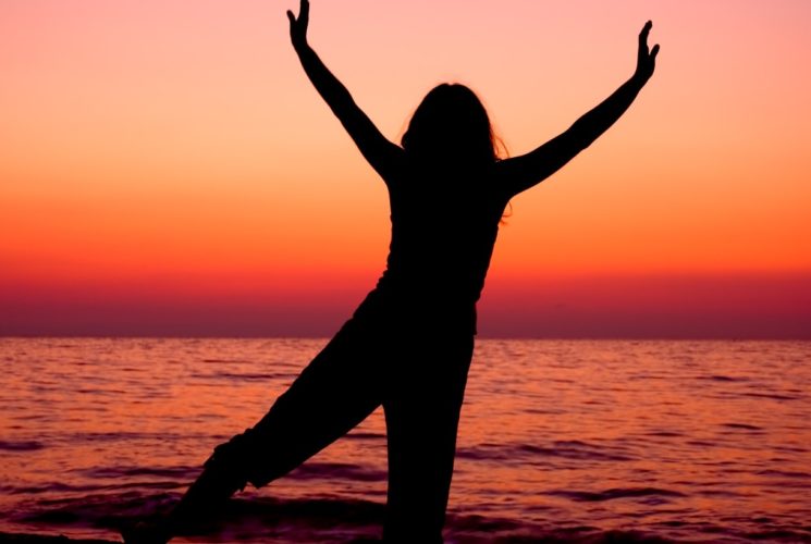 Silhouette of woman posing near body of water at sunset